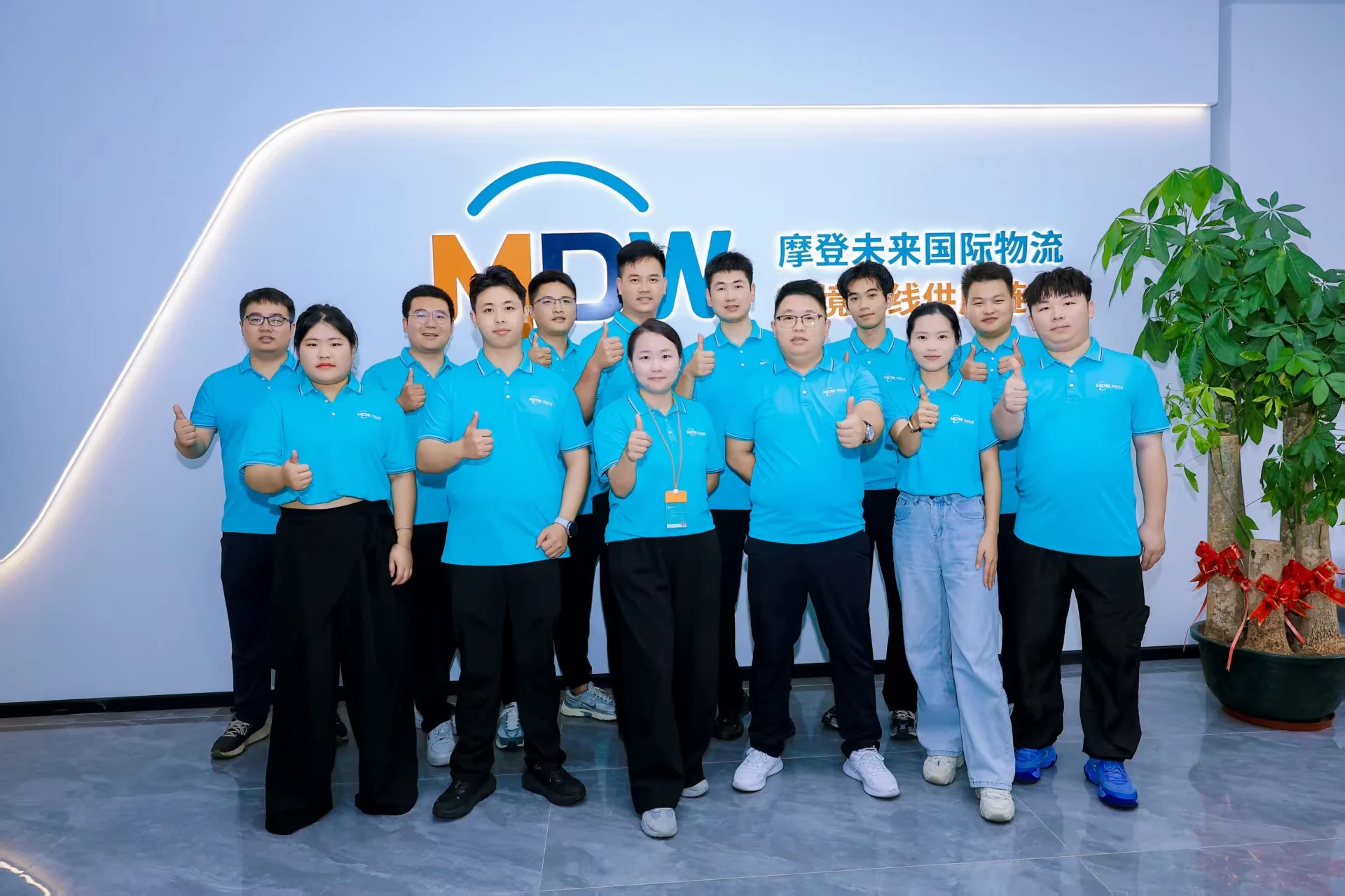 Modern Future Logistics Shenzhen office team in front of the company brand wall